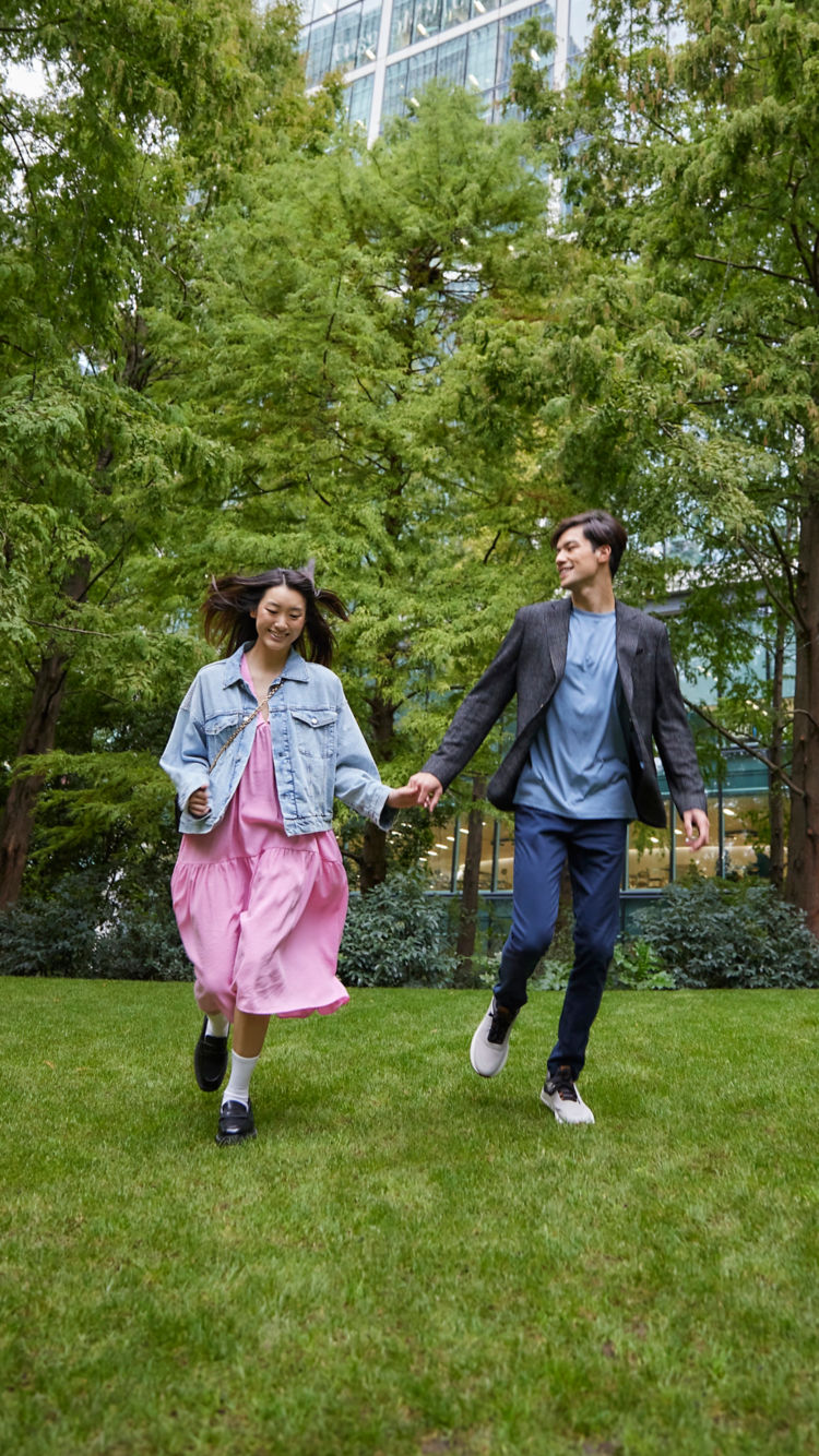 Happy Asian couple running in the park next to a high-rise building